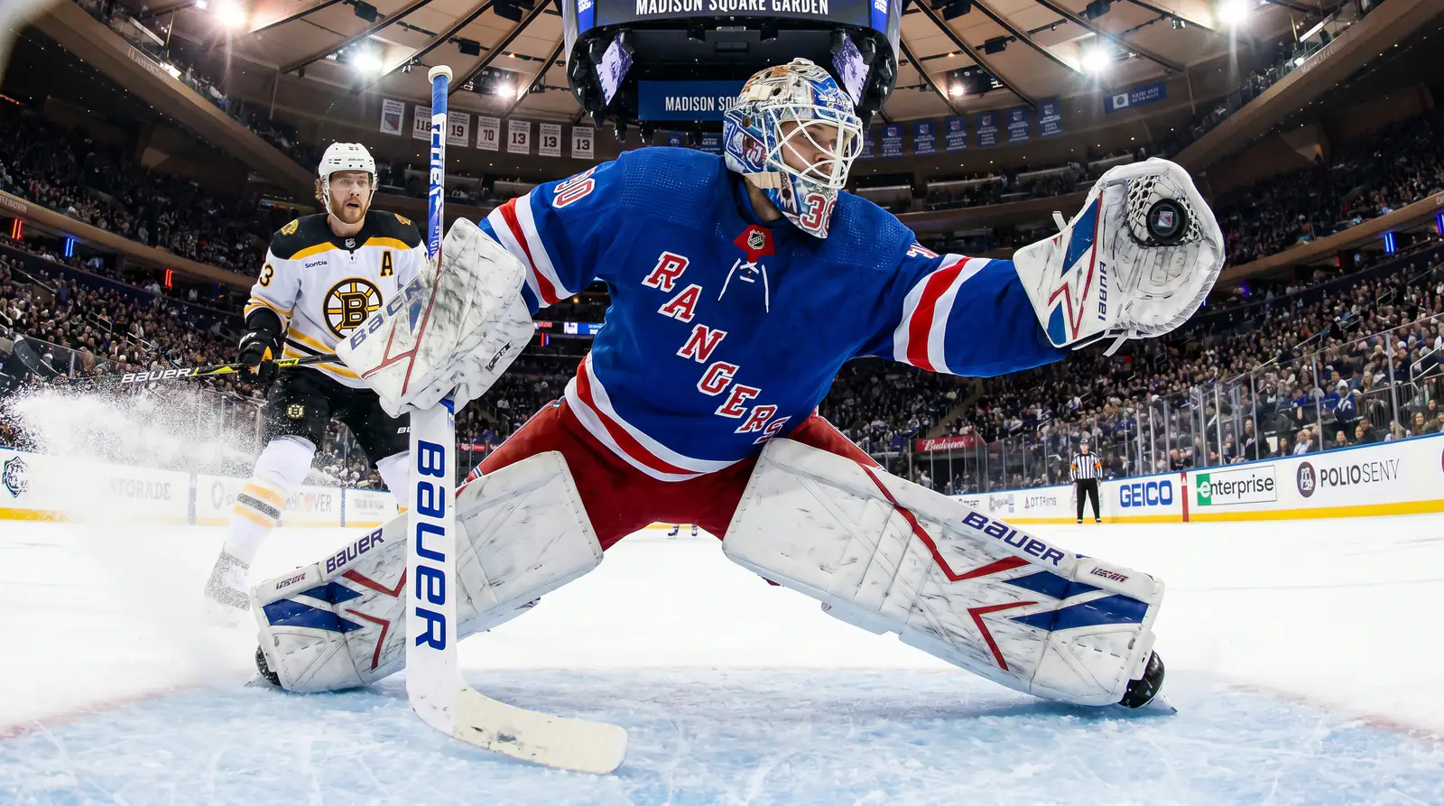 Goaltender making a key save during an NHL game with the puck deflecting off the pads